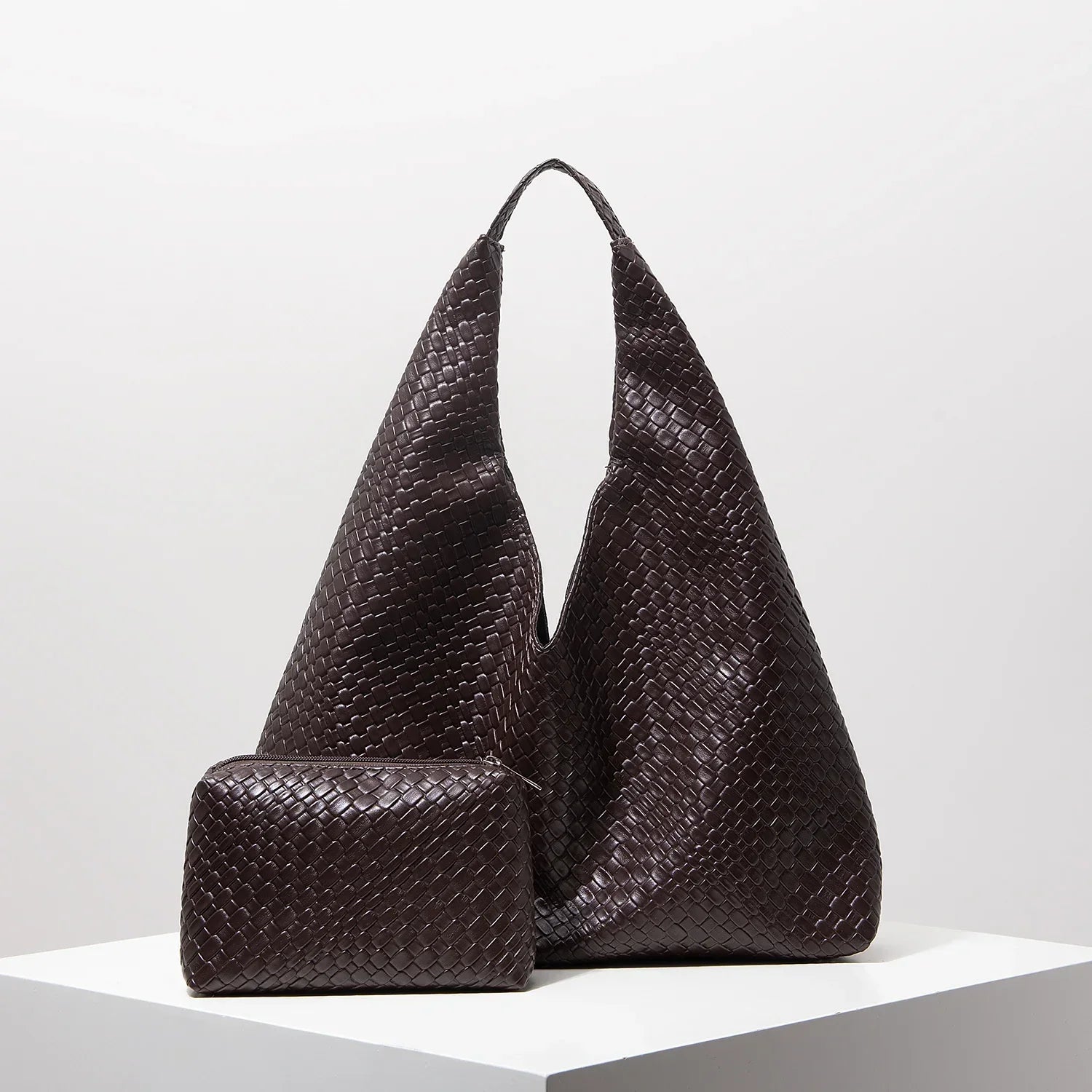 Bolsa feminina marrom de couro trançado com nécessaire combinando sobre base branca.