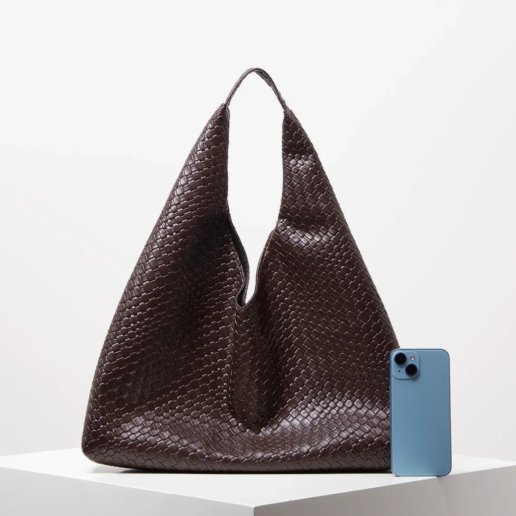 Bolsa grande marrom de couro trançado e celular azul sobre superfície branca