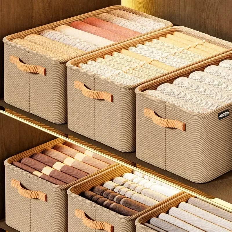 Caixas organizadoras bege em prateleira de madeira com roupas dobradas e organizadas.